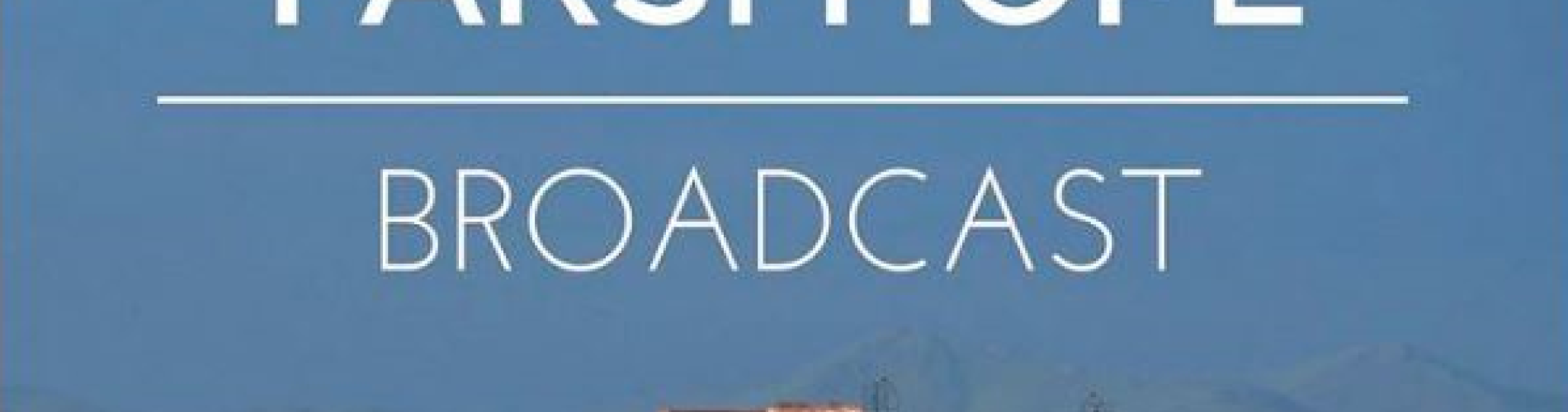 Rooftops with numerous satellite dishes against a blue sky and mountain background.