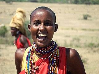 Smiling person wearing colorful beaded jewelry outdoors in a grassy landscape.