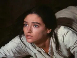 Woman with dark hair and white clothing looking up with a concerned expression.