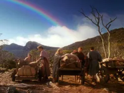 Group of people with carts under a rainbow in a scenic, mountainous landscape.